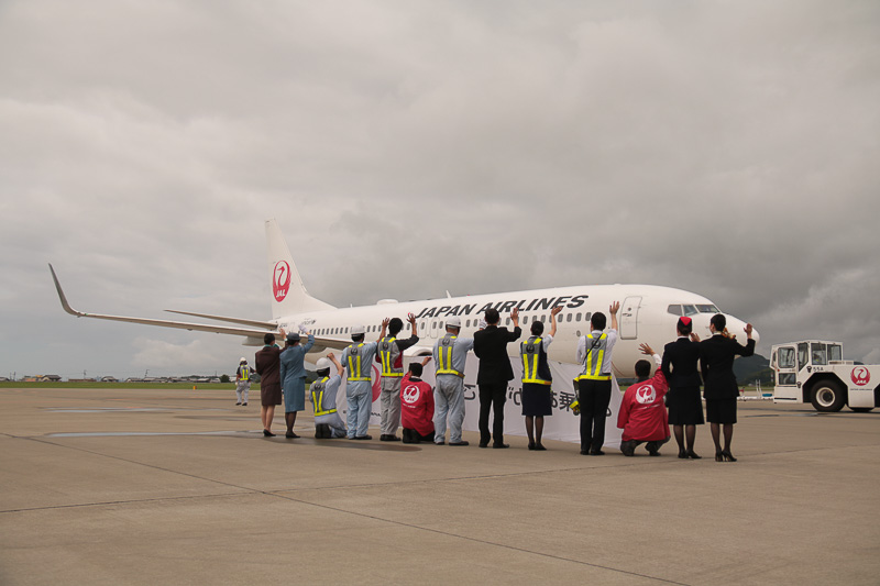 「ご搭乗ありがとうございます」の横断幕を持ってお見送りをするJALスタッフ