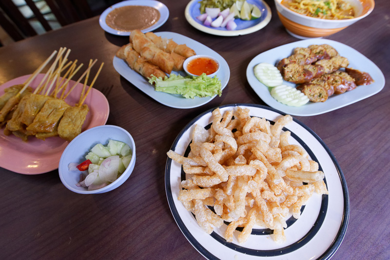 右下に見える揚げた豚皮や、その左に見えるタマネギなどをトッピングしたりする。左端は東南アジアでよく食べられる串焼き「サテー」