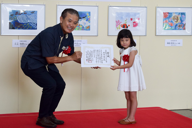 沖縄観光コンベンションビューロー賞を受賞した、早岡佐納（はやおかさな）さん（高知県在住、5歳）。プレゼンターは沖縄観光コンベンションビューロー 専務理事 前田光幸氏