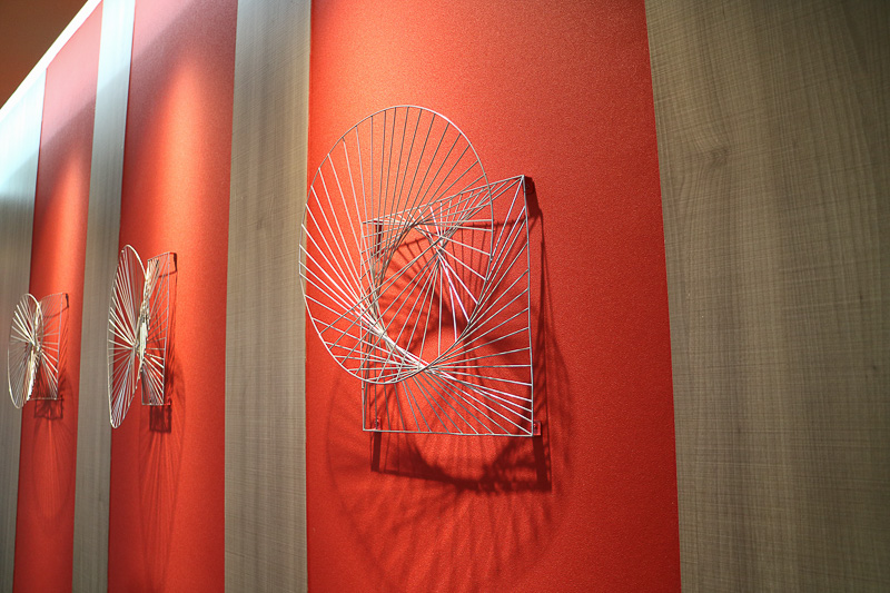 ラウンジスペースのアートワークは、マニラヤシが風に揺らぐイメージを表現したスチール素材のオブジェが、コーポレートカラーの赤色の上に飾られている