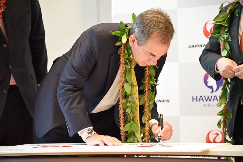 包括的業務提携契約に合意したことを祝いパネルに代表らが笑顔でサイン