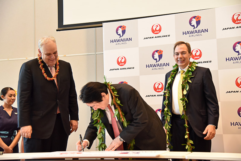 包括的業務提携契約に合意したことを祝いパネルに代表らが笑顔でサイン