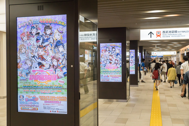 西武池袋線の池袋駅の地下1階改札への通路。サイネージが「ラブライブ！」のスマホゲーム一色。下にツアーの広告がある