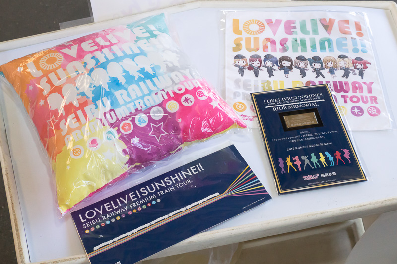 配布されたグッズ。清瀬赤目氏描き下ろしプレミアムトレインオリジナルクッション、清瀬赤目氏描き下ろしプレミアムトレインオリジナルハンカチ、シリアルナンバー入りプレミアムトレイン乗車記念プレート、記念切符