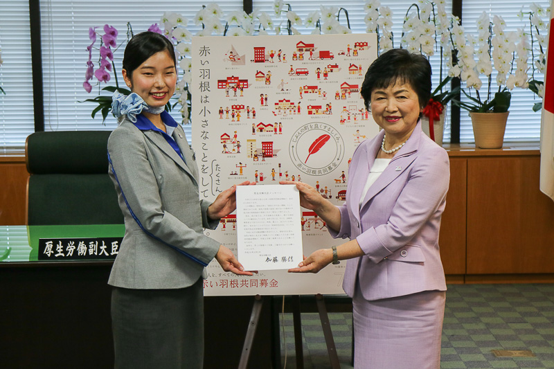 厚生労働省 副大臣 高木美智代氏が、厚生労働大臣である加藤勝信氏からのメッセージを代読し、全日本空輸株式会社 CA（客室乗務員）の菅野彩花氏に手渡した