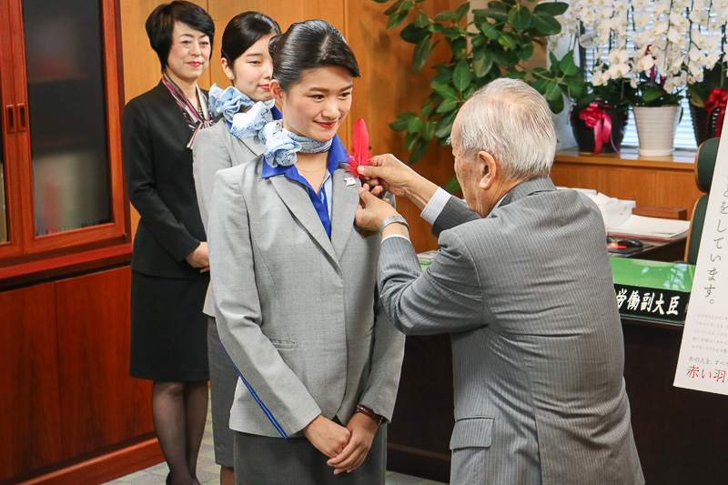 高木副大臣からCAの菅野彩花氏へ、斎藤会長からCAの上山聡子氏の胸元へ、赤い羽根が着けられた