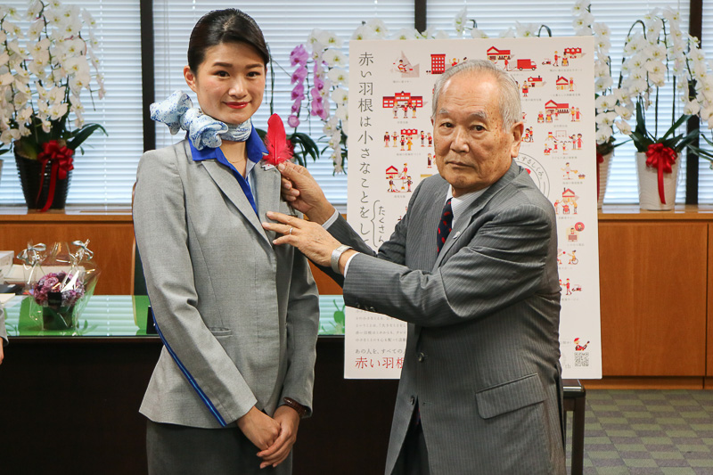 高木副大臣からCAの菅野彩花氏へ、斎藤会長からCAの上山聡子氏の胸元へ、赤い羽根が着けられた