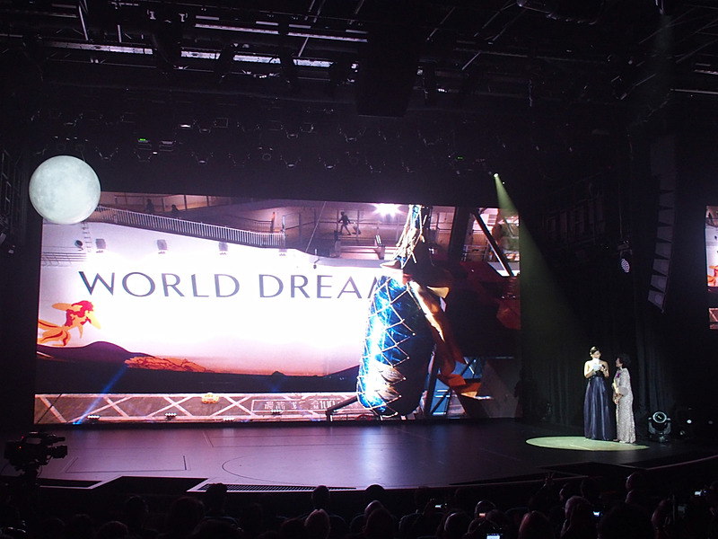 ステージにワールド ドリームの左舷船体船名部分と岸壁にセットしたシャンパンが映し出された