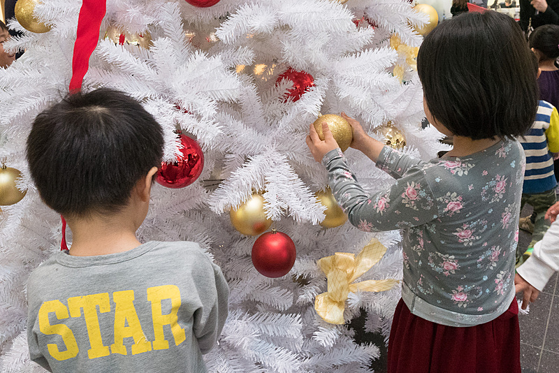 大きなクリスマスツリーへゴールドや赤色のボールを楽しそうに飾り付け