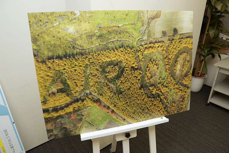 植樹した森林を2017年10月にドローンで撮影した写真パネル。常緑樹と落葉樹の色の違いでAIR DOの文字が浮かび上がる