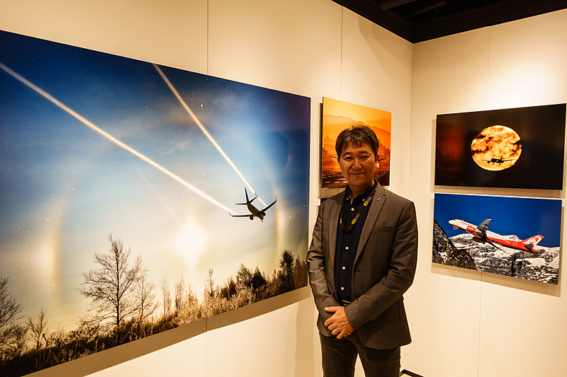 中野耕志氏、主に旅客機の作品が飾られているエリアで。向かって左が新千歳空港付近で撮影した作品