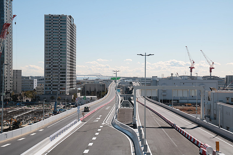 10号晴海線の豊洲入口と晴海入口は並んでいる。現在の路面のマーキングは豊洲入口側が主線となっているが、追々は晴海入口側を主線に変更するとのこと。東京湾に向かって右手に見えるクレーン群は、2020年東京オリンピック・パラリンピックの競技場の建設機材