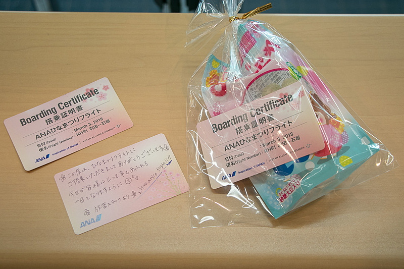 手書きのメッセージを書き込んだ搭乗証明書を添えたひなあられを乗客に手渡し