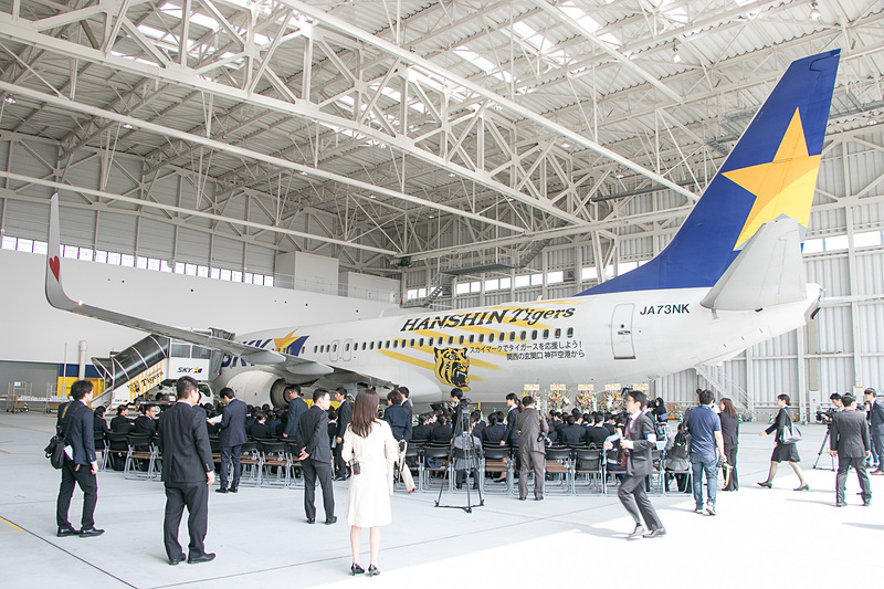 神戸空港の格納庫に集まる新入社員たち。入社式は「タイガースジェット」の前で行なわれた
