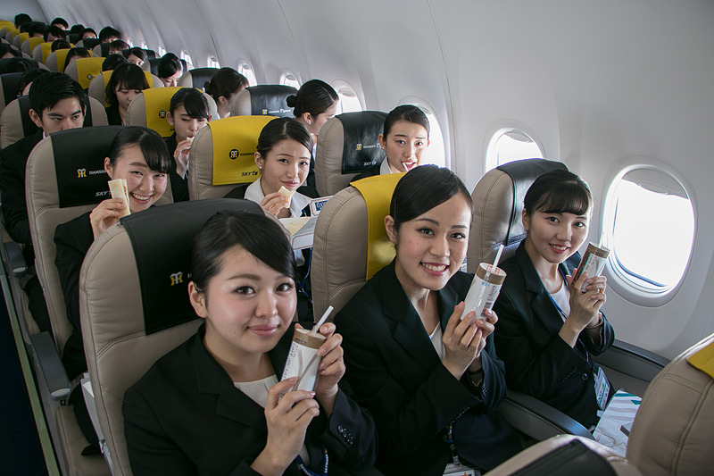 配られたサンドイッチのお弁当を食べながら空の旅を楽しむ新入社員。お世話になった人事部長との記念撮影を求める人も多かった