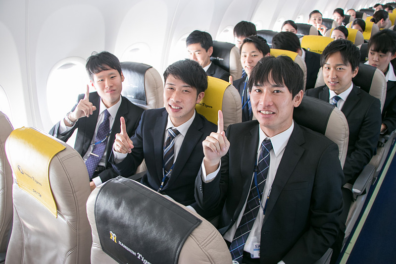 配られたサンドイッチのお弁当を食べながら空の旅を楽しむ新入社員。お世話になった人事部長との記念撮影を求める人も多かった