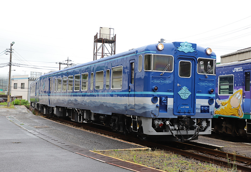 撮影時は曇天のため深い青に見えたが、晴天だと異なった趣になりそうだ。隣に停車しているのは境港線 鬼太郎列車「子泣き爺車両」