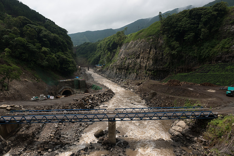 立野ダム建設予定地の上流側にある橋からの眺め。前方奥にある低い仮設橋がダムの建設予定地、右側の崖の特異な形状が柱状節理と呼ばれるもの。左下に見えるトンネルは仮排水路トンネルと呼ばれるもので詳しくは後述する