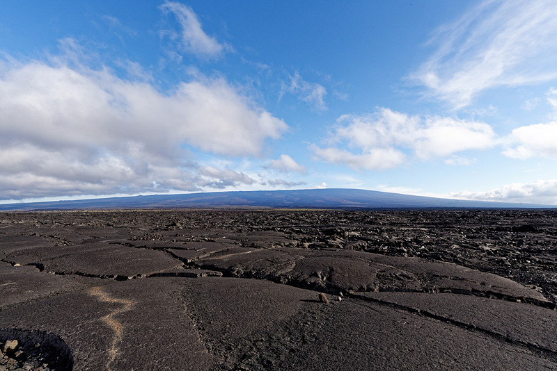 遠くに見えるのがマウナロア山。溶岩が冷えて固まることでできた黒々とした岩石が広がっている