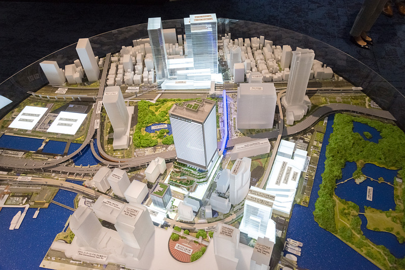 模型による「（仮称）竹芝地区開発計画」の全体イメージ。奥が浜松町側、手前が竹芝側で、竹芝側の高いビルが業務棟となる。青く光っているのが歩行者デッキの浜松町と業務棟とを結ぶ部分