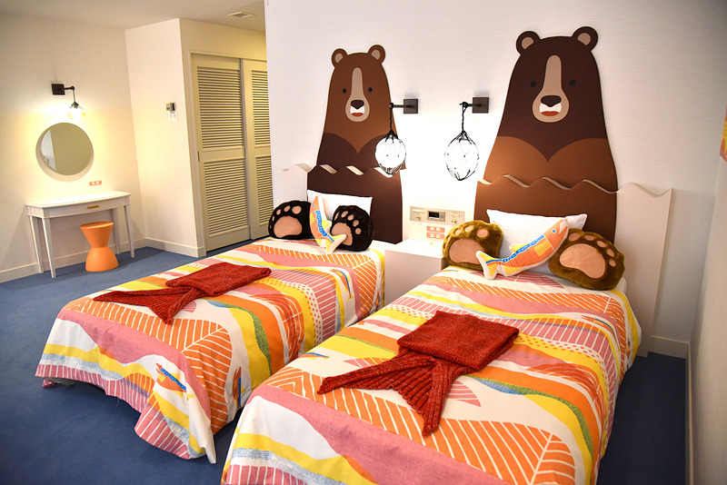 熊が川で遡上する鮭を狙う様子をユーモアたっぷりに表現。ミニ鮭クッションもちょこん