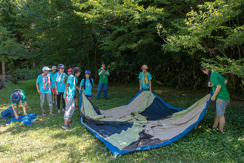 キャンプ場へ到着。さっそくテント張りが開始される。女子チームはみんな同じテントとなるので全員で作業。サポートスタッフが声をかけずとも、子供たちは自分でやることを探して動いているので、初めて張るテントも短時間で設営完了！