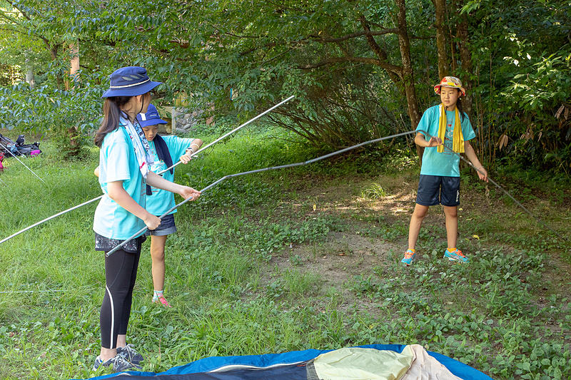 キャンプ場へ到着。さっそくテント張りが開始される。女子チームはみんな同じテントとなるので全員で作業。サポートスタッフが声をかけずとも、子供たちは自分でやることを探して動いているので、初めて張るテントも短時間で設営完了！