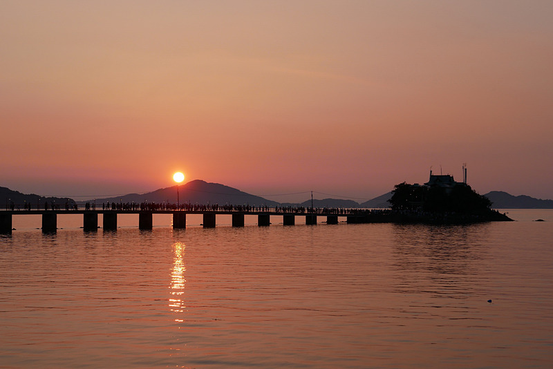 夕暮れ時、津嶋神社の奥に沈む夕日に赤く染められた空や海と、津嶋神社のシルエットも必見の美しさだ