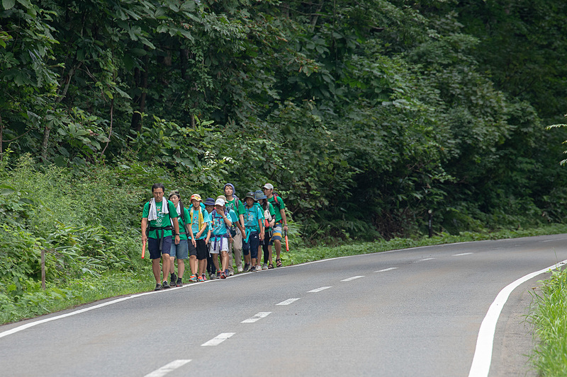 国道459号を歩くメンバー。車道と歩道が分かれていない難所なので、先頭と最後尾の大人はクルマへの合図をするための誘導棒を持つ