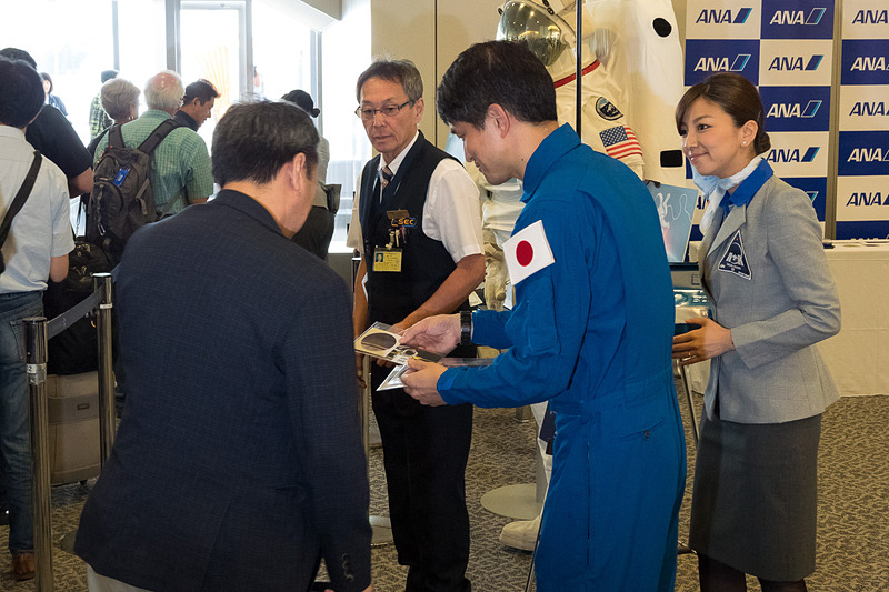 飛行機のまわりでは「宇宙日本食」も入った機内食を積み込むフードローダーなどによる出発準備が進むなか、大西 宇宙飛行士らが搭乗客に搭乗証明書やステッカーを配布