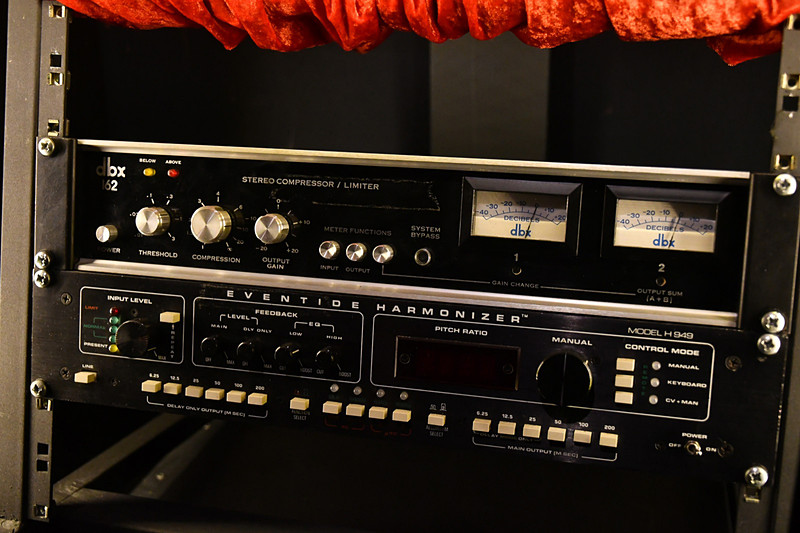 上段がdbx社製のコンプレッサー（音を圧縮して整え、迫力が増す効果を持つ）である162というモデル。下段がイーブンタイド社製のハーモナイザー（任意で原音からずらした音階の音を出力しハモり効果を出す）H949。説明ボードによると、かなり重要な役割を担っていたことが分かる