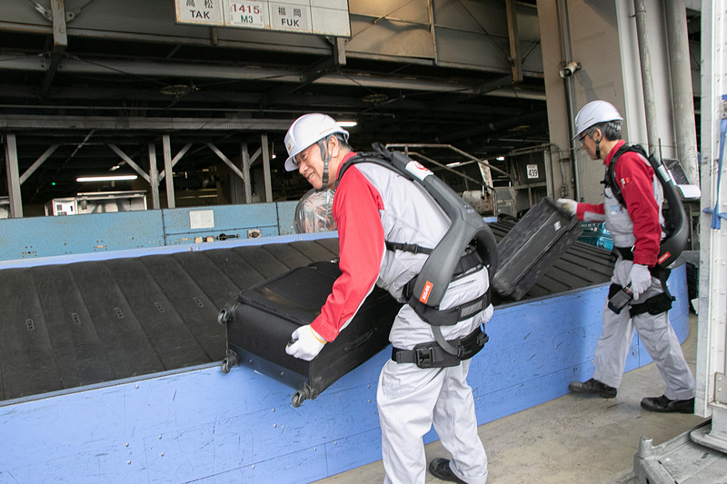 JALスタッフが羽田空港の荷捌き場で「ATOUN MODEL Y」を着用して、ベルトコンベアからコンテナへの積み込み作業を行なう様子を公開した