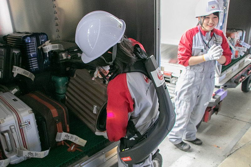 JALスタッフが羽田空港の荷捌き場で「ATOUN MODEL Y」を着用して、ベルトコンベアからコンテナへ手荷物の積み込み作業を行なう様子を公開した