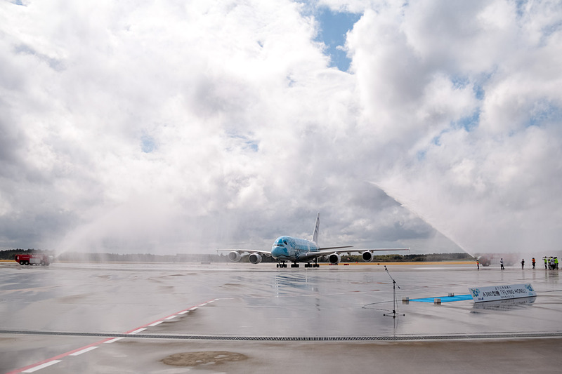 成田空港はウォーターキャノンで同機の到着を歓迎。直前まで降っていた雨は上がっていたが、注意報が出るほどの強風が吹いていたので、放水車からの水はミストシャワーのカーテンのよう