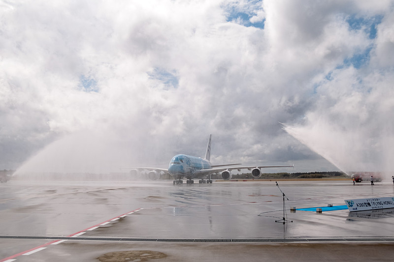成田空港はウォーターキャノンで同機の到着を歓迎。直前まで降っていた雨は上がっていたが、注意報が出るほどの強風が吹いていたので、放水車からの水はミストシャワーのカーテンのよう