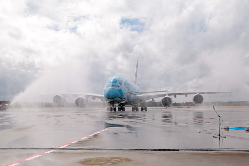 成田空港はウォーターキャノンで同機の到着を歓迎。直前まで降っていた雨は上がっていたが、注意報が出るほどの強風が吹いていたので、放水車からの水はミストシャワーのカーテンのよう