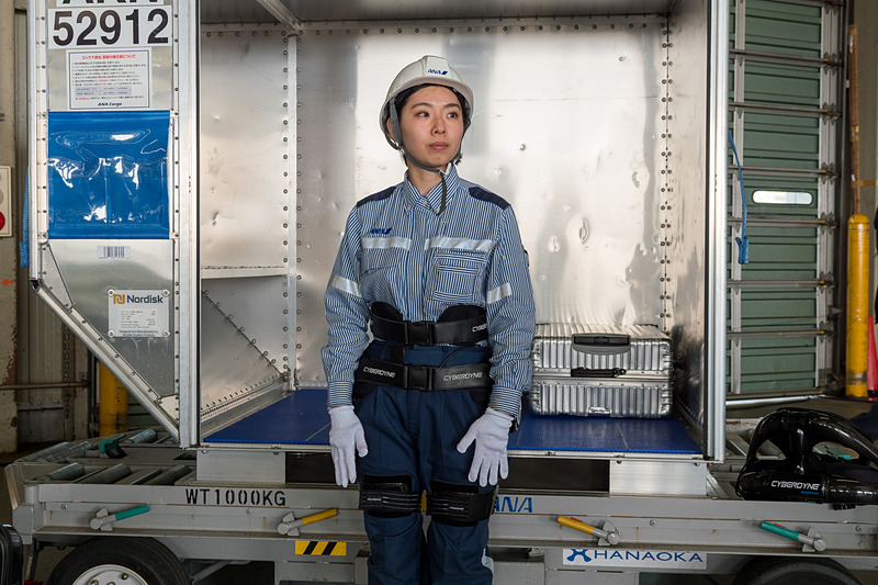 サイバーダイン製のロボットスーツ「HAL」。10kgのおもりを入れたスーツケースを軽々とコンテナに積んでいく様子をデモ。デモをした女性スタッフは「重い荷物を連続して持つことが多いので腰への負担が大きかった。ロボットスーツを使うことで、半分ぐらいの力で持ち上げられる」とコメント