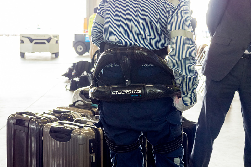 サイバーダイン製のロボットスーツ「HAL」。10kgのおもりを入れたスーツケースを軽々とコンテナに積んでいく様子をデモ。デモをした女性スタッフは「重い荷物を連続して持つことが多いので腰への負担が大きかった。ロボットスーツを使うことで、半分ぐらいの力で持ち上げられる」とコメント