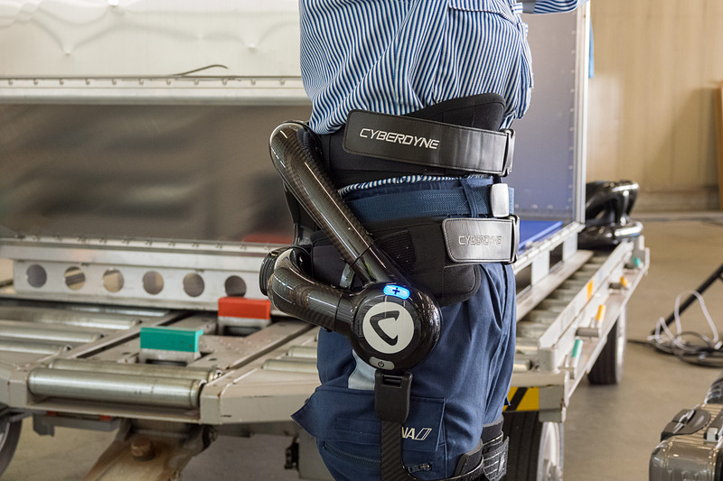 サイバーダイン製のロボットスーツ「HAL」。10kgのおもりを入れたスーツケースを軽々とコンテナに積んでいく様子をデモ。デモをした女性スタッフは「重い荷物を連続して持つことが多いので腰への負担が大きかった。ロボットスーツを使うことで、半分ぐらいの力で持ち上げられる」とコメント