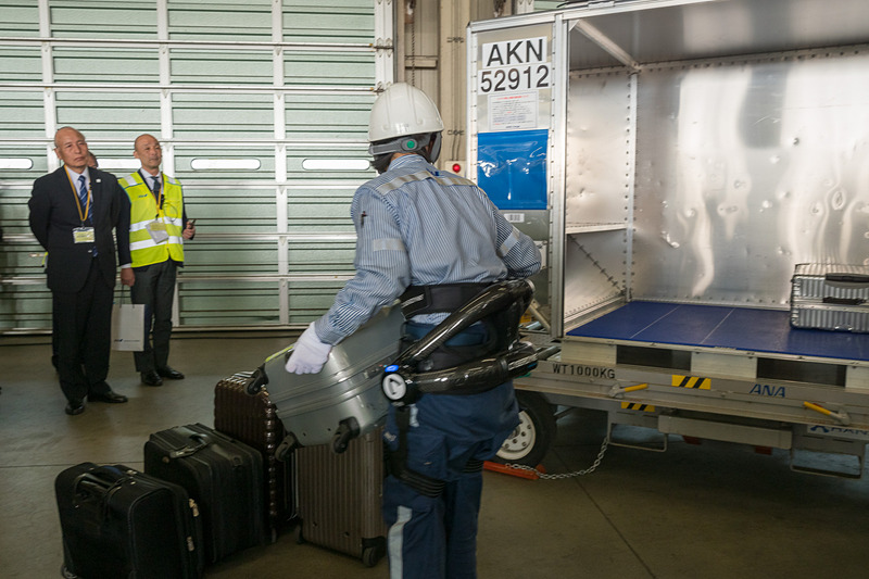 サイバーダイン製のロボットスーツ「HAL」。10kgのおもりを入れたスーツケースを軽々とコンテナに積んでいく様子をデモ。デモをした女性スタッフは「重い荷物を連続して持つことが多いので腰への負担が大きかった。ロボットスーツを使うことで、半分ぐらいの力で持ち上げられる」とコメント