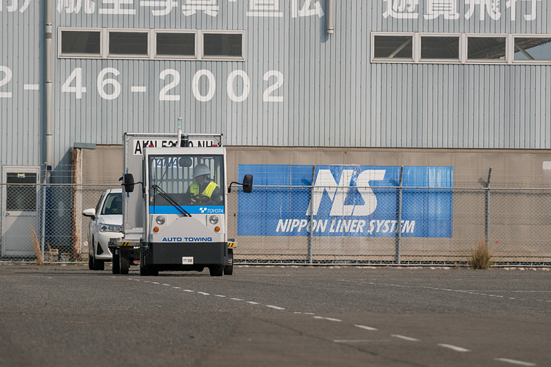コンテナが乗ったドーリーを運搬する自動運転トーイングトラクター。デモでは1台のドーリーを引いているが最大6台を連結するという