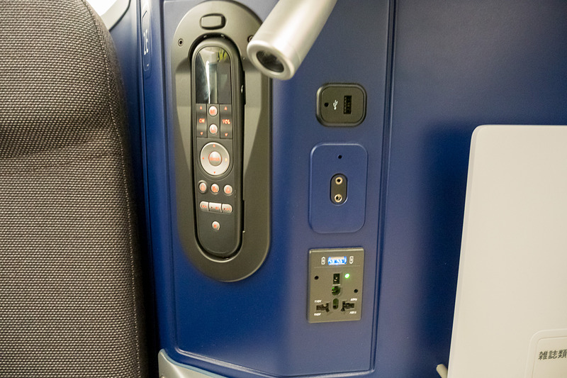 サイドテーブルに機内エンタテイメント用コントローラ、ノイズキャンセリングヘッドフォン端子、電源類。USB電源を2つ備えるのも特徴の一つ