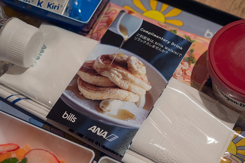 コラボレーション機内食のトレイに乗るカード。bills Waikikiに持参して料理を楽しむ際に、ウェルカムドリンクをサービスしてもらえる