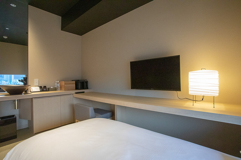 壁にはテレビ。机がベッド横まで伸びているので、ベッドに腰掛けてPC作業もできる