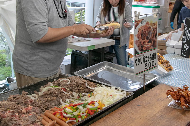 アメリカ料理の屋台のイチオシは「チーズステーキドック」（700円）。鉄板で焼いたチキンにトロ～リチーズが美味。「ワタリガニから揚げ」（500円）はカラごとバリバリ食べられる食感も美味しい一品