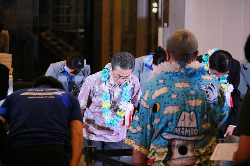 搭乗者をゲートで迎え一礼する平子社長と石田成田空港支店長。ディスプレイにはラニの画像も表示。フライト時間は7時間20分、現地は曇り、気温は23℃（摂氏）と表示されていた