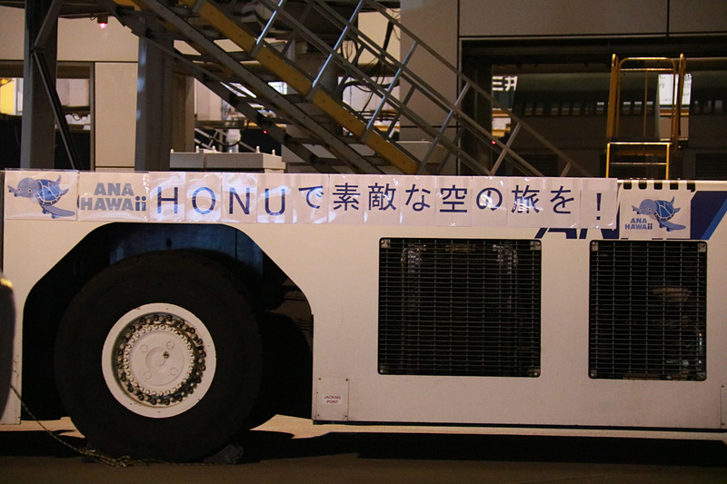 ラニのエンジンの向こうに見えるのは、FLYING HONU 2号機のカイ。機長が地上の見送りに向かい手を振ってプッシュバック。トーイングカーにもメッセージが貼られていた