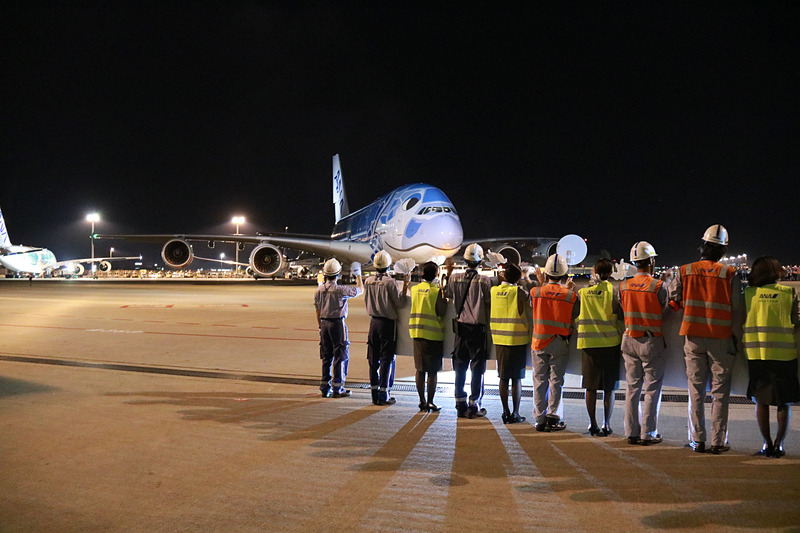ラニのエンジンの向こうに見えるのは、FLYING HONU 2号機のカイ。機長が地上の見送りに向かい手を振ってプッシュバック。トーイングカーにもメッセージが貼られていた