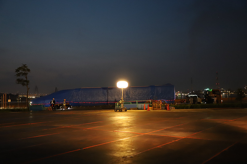 トレーラーが慎重にバックし、新幹線車両のノーズ部分から敷地内に進入する