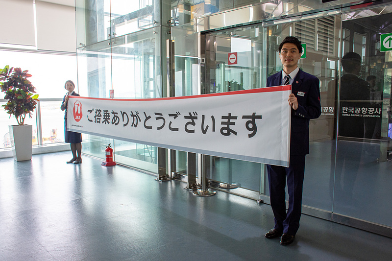 阿部孝博氏らがゲート前で乗客一人一人に笑顔で記念品を手渡した